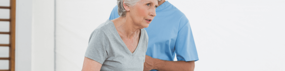 Older woman struggling to walk between parallel bars